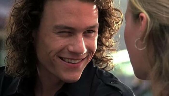 Young man with curly hair smiling and winking at a woman in a close-up scene from a worst movie tropes quiz.