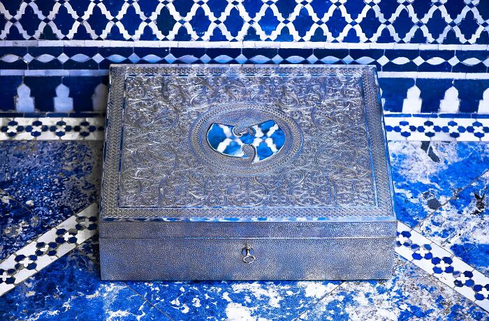 Ornate silver collectible box with intricate designs displayed on a blue patterned surface, a high-value collectible item.