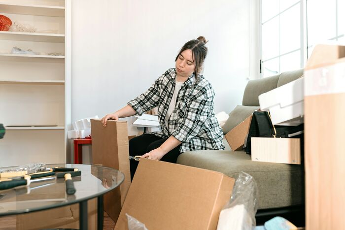 Young woman organizing and unpacking boxes at home, illustrating small daily wins from feminists in everyday life.