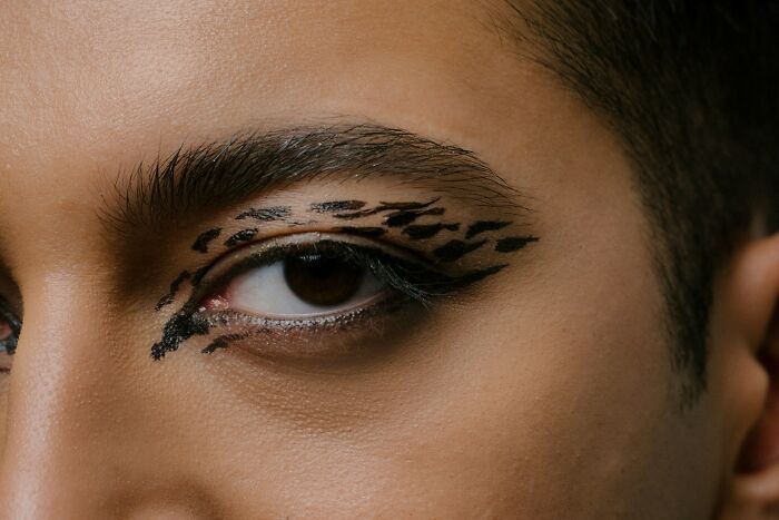 Close-up of a person's eye with unique black patterns resembling mysterious body quirks on the skin around the eye.