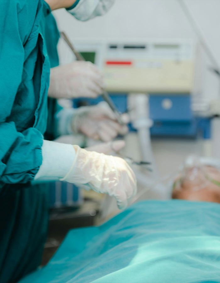 Autopsy tech wearing gloves performing an examination in a medical setting with patient on the table.