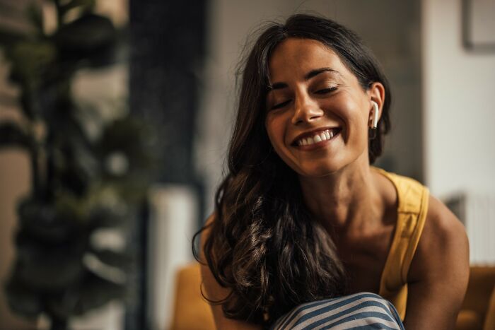 Young woman smiling and listening with earbuds at home, reflecting on people who ran away from home stories. - 18