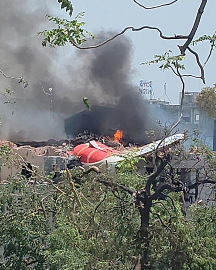 Wreckage of Air India plane crash with smoke and flames rising above building, showing aftermath of the disaster. - 3