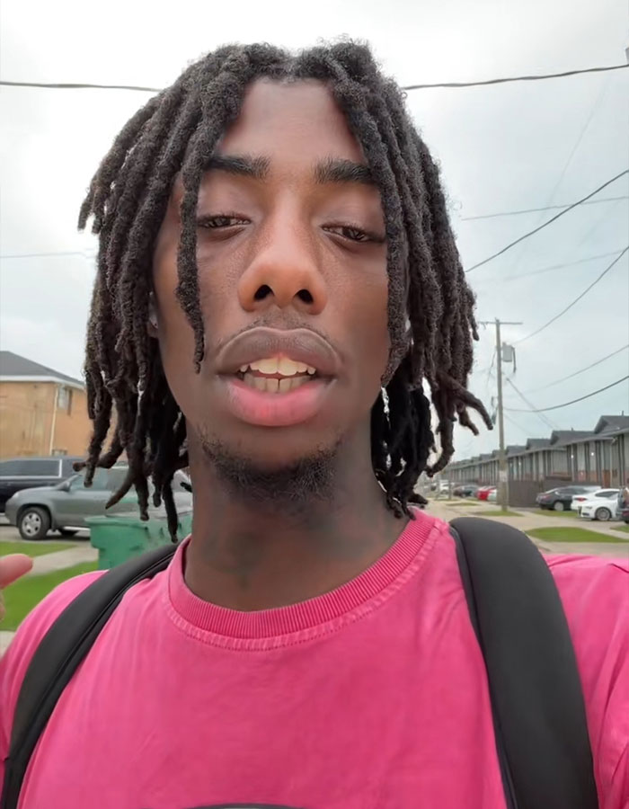 Young man wearing a pink shirt and backpack outdoors, expressing frustration related to plane passenger seat dispute. Young man wearing a pink shirt and backpack outdoors, expressing frustration related to plane passenger seat dispute.