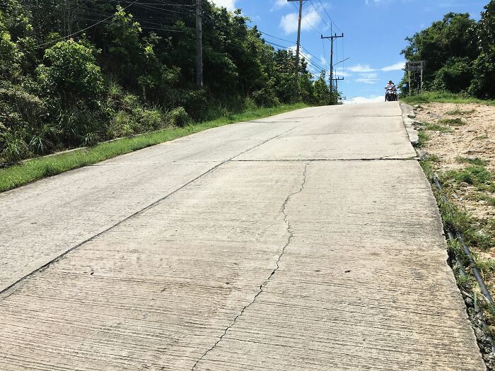 Steep concrete hill beside greenery with a person on a motorcycle traveling up under blue sky, travelers share surprising insights.