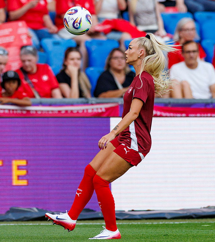 Female footballer with blonde ponytail in red kit controlling the ball during a match, showcasing stunning transformation on field.