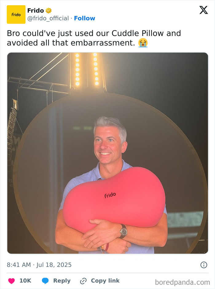 Man smiling and holding a large red Frido pillow in a lit studio, related to brands making fun of CEO caught cheating.