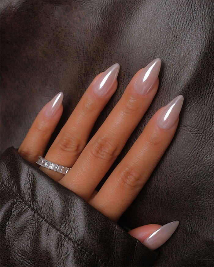 Hand with glossy n**e almond nails and a silver ring resting on dark brown leather fabric, showcasing almond nails trends.