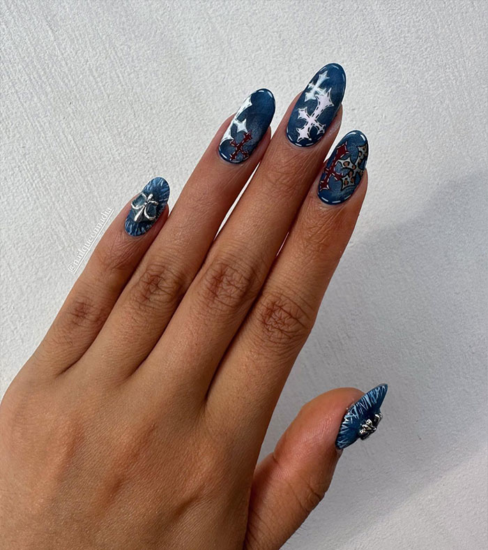 Close-up of almond nails with blue and metallic designs featuring star patterns and 3D embellishments.
