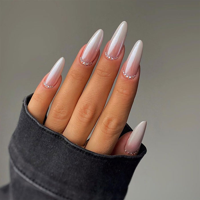 Almond nails with a soft pink gradient and rhinestone accents on fingers against a neutral background.