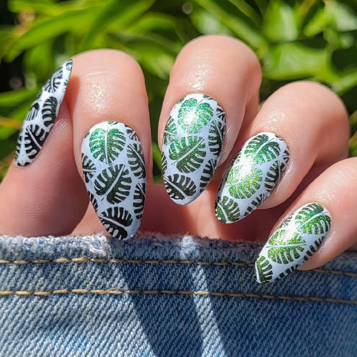 Almond nails with green tropical leaf design on white background, showcasing trendy nail art for 2025.