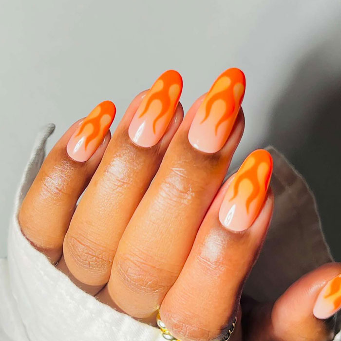 Hand with almond nails featuring bright orange flame nail art on a n**e base showcasing almond nails trends.