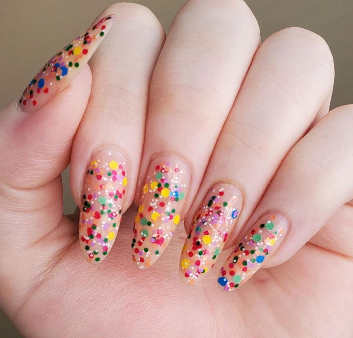 Almond nails with clear polish and colorful confetti dots creating a festive and trendy nail design for 2025.