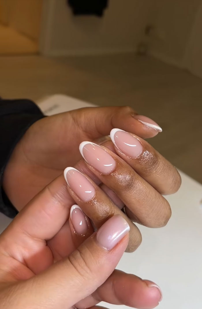 Close-up of almond nails with a glossy n**e base and white French tips showcasing 2025 nail trends.
