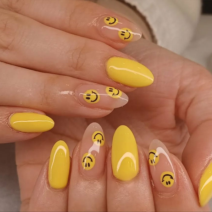 Glossy yellow almond nails with clear tips featuring playful smiley face designs, showcasing trendy almond nails for 2025.