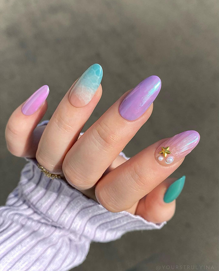Almond nails with pastel purple, teal, and ocean wave designs featuring 3D star and pearl accents on a hand.