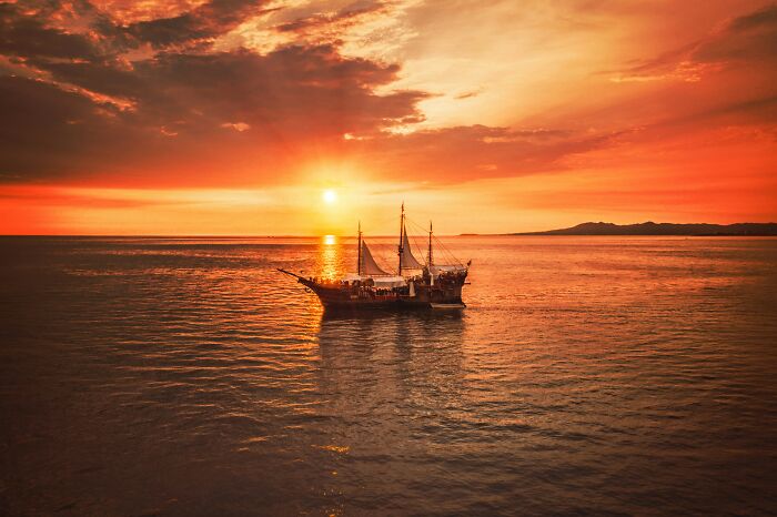 Sailing ship on calm sea during a dramatic sunset, evoking scenes from crazy but real historical events.