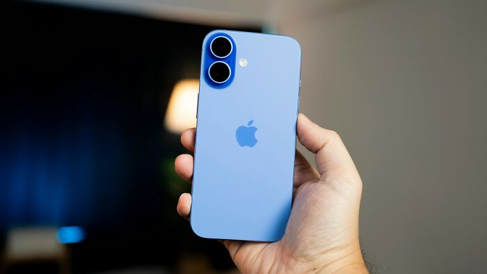 Hand holding a blue iPhone against a blurred background illustrating trends leading to overconsumption concerns. - 14