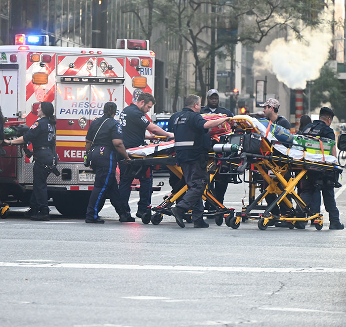 NYPD cop fatally shot, surrounded by emergency responders and paramedics with stretchers near an ambulance on city street.