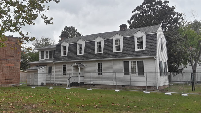 Historic US school building surrounded by fencing as archaeologists explore a forgotten cellar with mysterious artifacts beneath it.