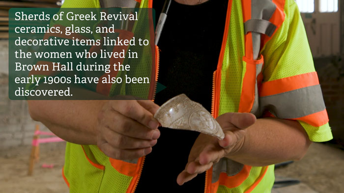 Archaeologist holds sherd of Greek Revival ceramic found among mysterious artifacts in forgotten cellar beneath historic US school.