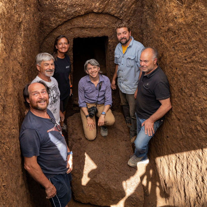 Archaeologists standing inside a 2,600-year-old tomb in Italy near the entrance to a mysterious burial chamber.