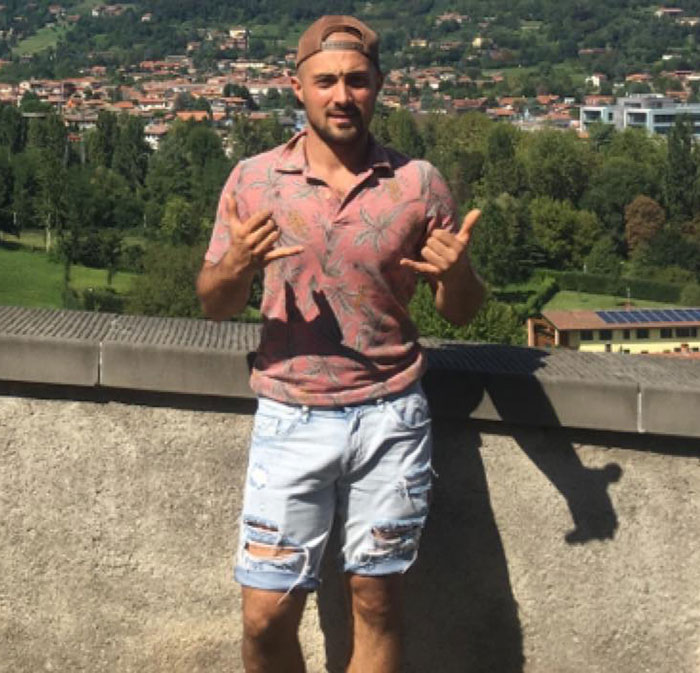 Young man in a pink shirt and ripped shorts posing outdoors with a scenic background, related to man sucked into plane engine.