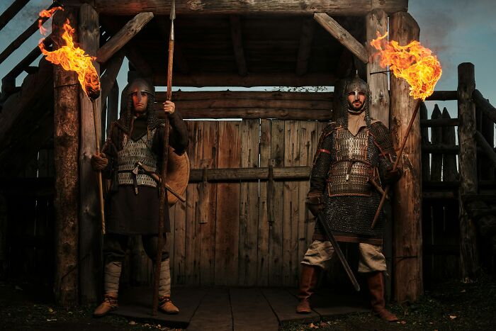 Two medieval warriors holding flaming torches standing guard in front of a wooden gate.