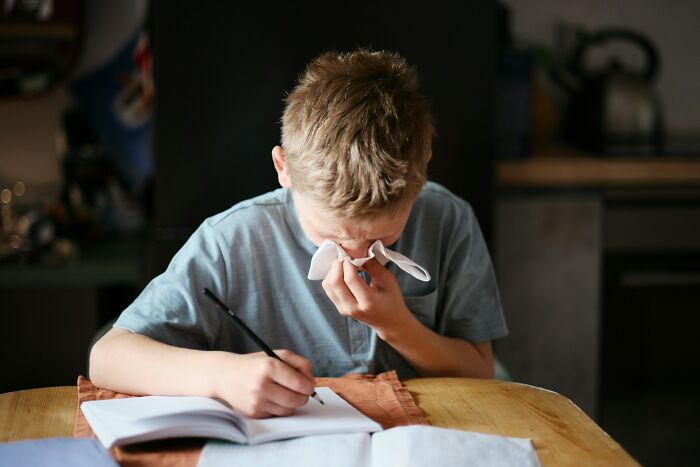 Young boy wiping nose with tissue while writing in notebook, illustrating extreme parenting punishments and kids left alone too long.