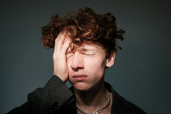 Young man with curly hair holding his face in pain, illustrating mysterious body quirks people can’t find answers for