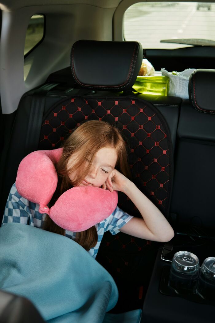 Young girl asleep in car seat with neck pillow and blanket, reflecting neglect and harsh parenting punishments.