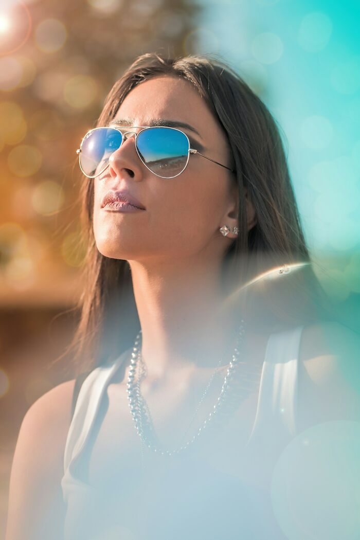 Woman wearing reflective sunglasses and a chain necklace, captured in soft light highlighting mysterious body quirks.
