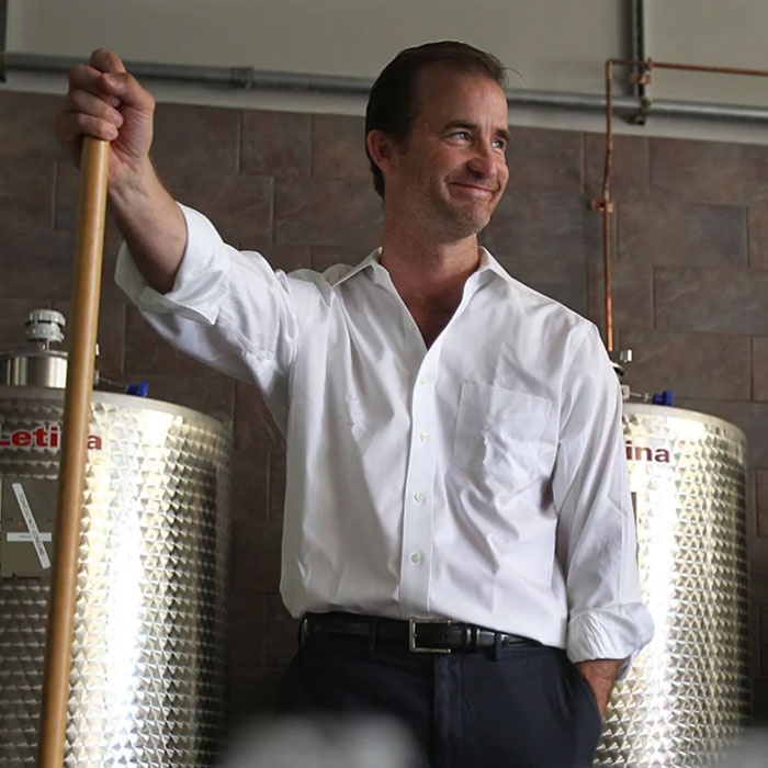 Man in white shirt standing by industrial tanks, related to Coldplay cheating scandal HR executive and Boston wealthy family connections. - 8