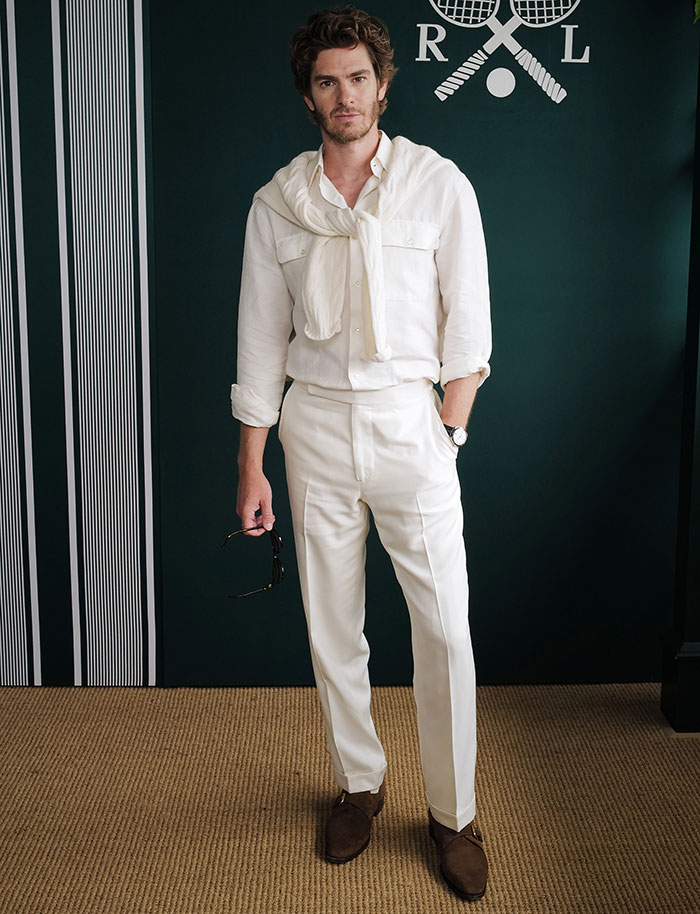 Man in white shirt and pants holding sunglasses, showcasing stylish Wimbledon 2025 celebrity looks at an indoor event.