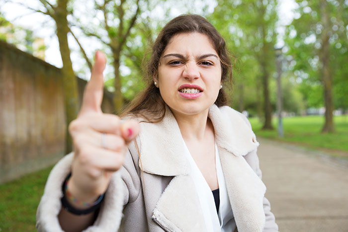 Angry young woman outdoors pointing finger, expressing frustration related to racist switch and family conflict.