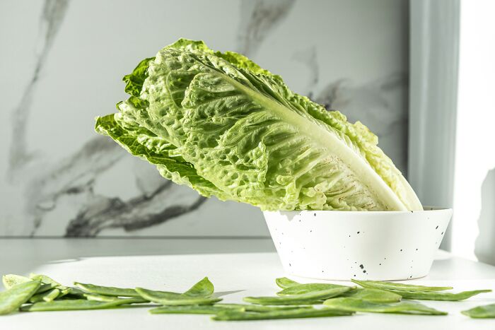 Fresh romaine lettuce leaves in a white bowl with scattered leaves, related to McDonald's employees' bizarre experiences.