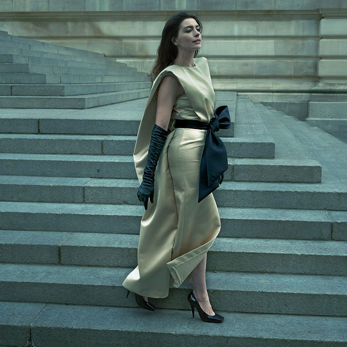 Anne Hathaway posing on stone steps in elegant gown with black gloves and bow in a Vogue cover photoshoot setting. Anne Hathaway posing on stone steps in elegant gown with black gloves and bow in a Vogue cover photoshoot setting.