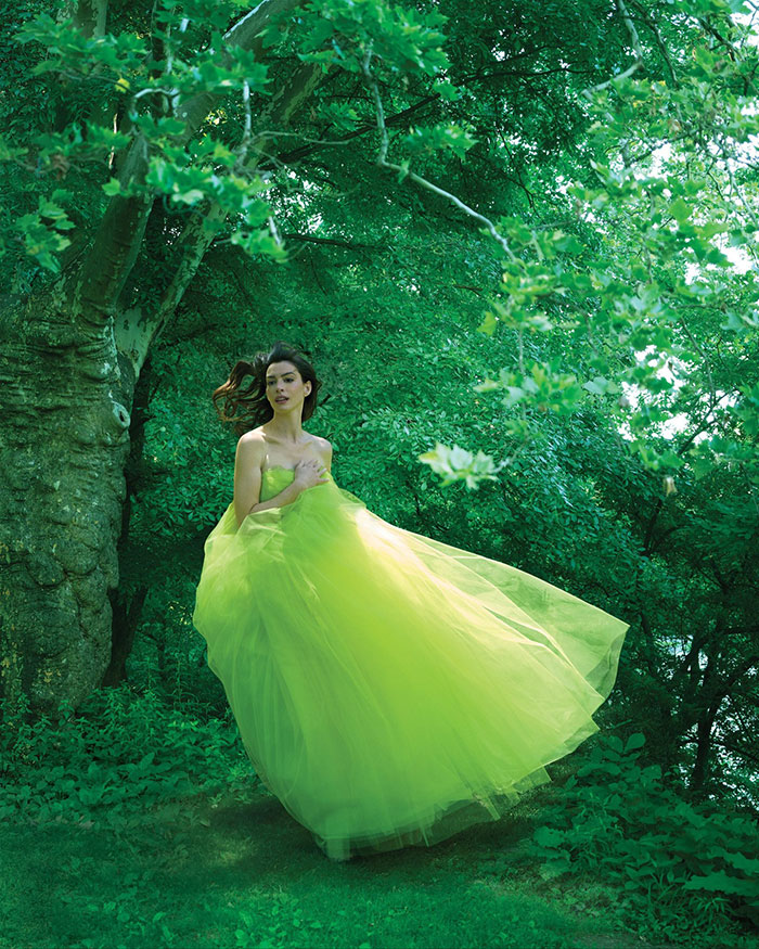 Woman in a flowing green dress posing in a forest setting for a Vogue photoshoot criticized by fans about Anne Hathaway. Woman in a flowing green dress posing in a forest setting for a Vogue photoshoot criticized by fans about Anne Hathaway.