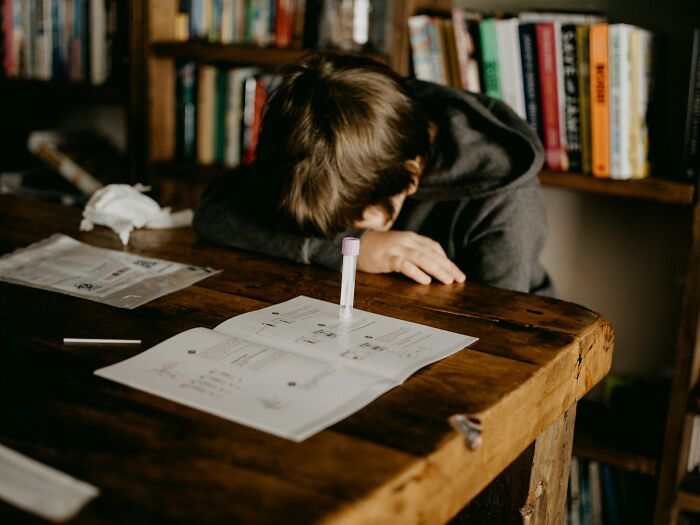 Child sitting alone at wooden table with head down, illustrating extreme parental punishment and neglect risks.