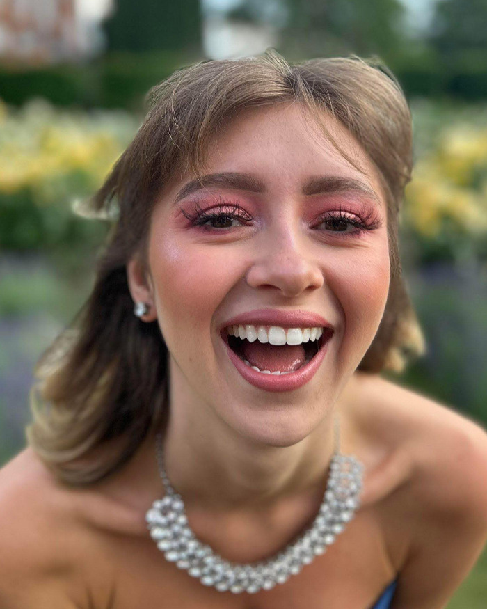 Young woman smiling outdoors wearing a pearl necklace, related to story about 23YO anti-vax woman refusing chemotherapy.