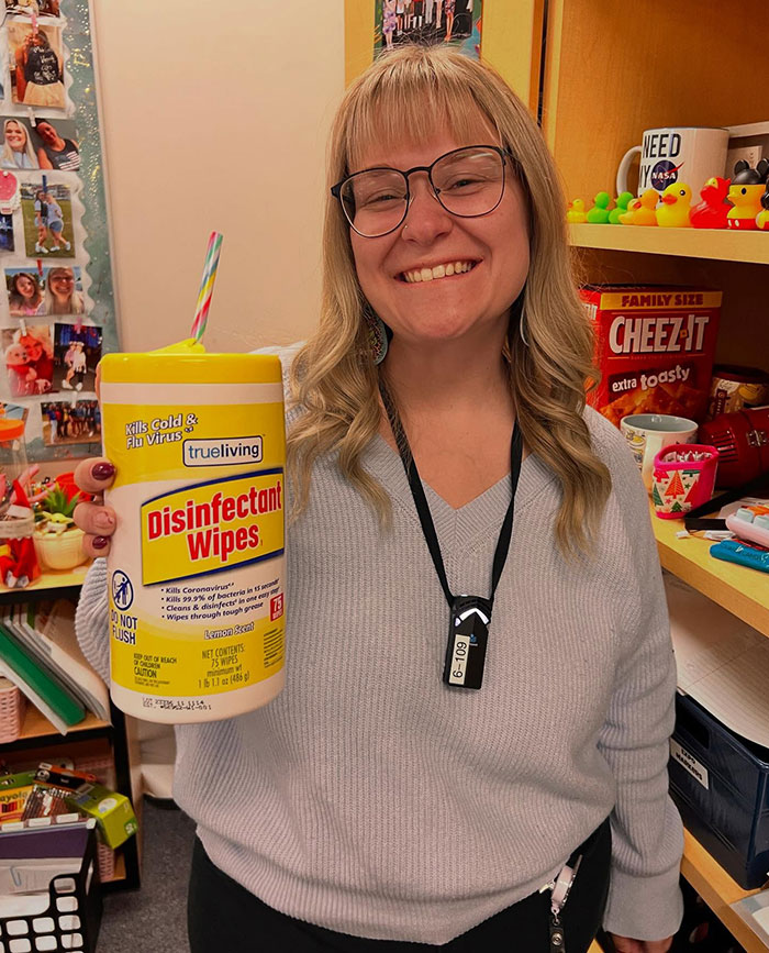 Woman smiling and drinking from a disinfectant wipes container with a colorful straw in a playful office setting