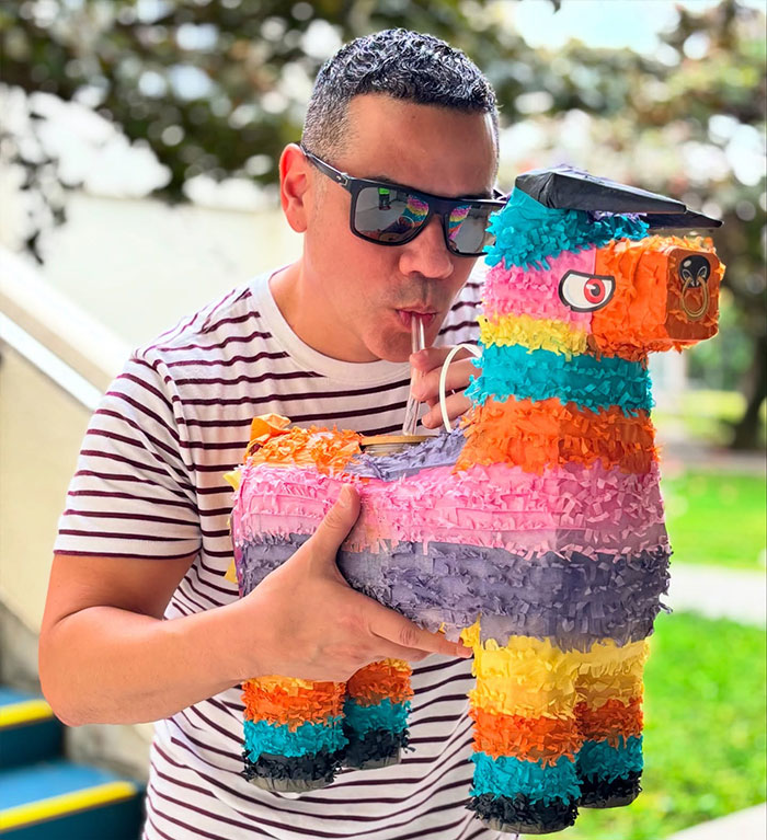 Man in sunglasses sipping drink from colorful llama-shaped creative sipper outdoors, showcasing unique drinking container idea.