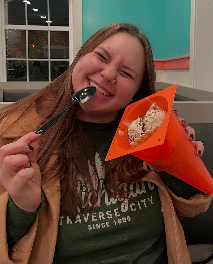 Young woman smiling and eating ice cream from a traffic cone, showcasing creative sippers using anything but a cup.