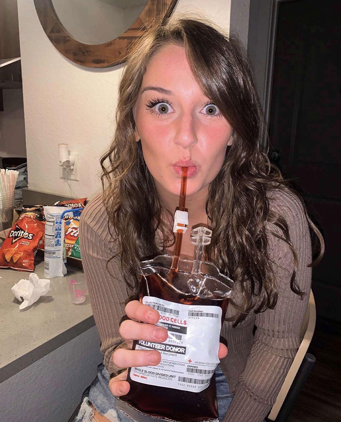 Young woman drinking with a straw from a novelty blood bag, showcasing creative sippers using unusual drink containers.