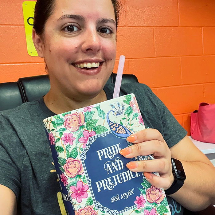 Woman smiling while sipping from a book with a floral cover using a straw, showcasing creative sippers idea.