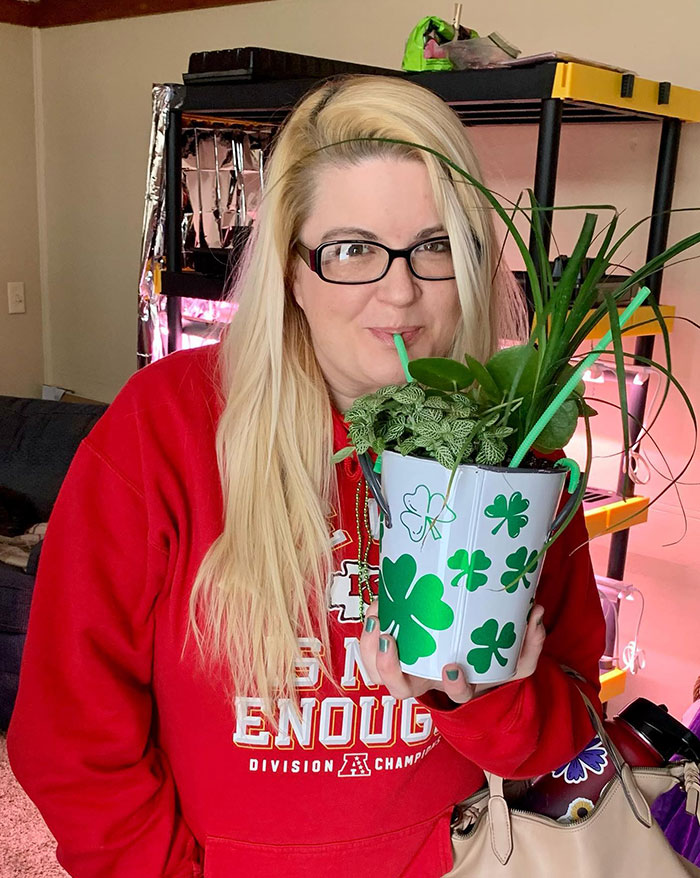 Woman sipping drink using straws from a decorative bucket filled with plants, showcasing creative sippers not using cups.