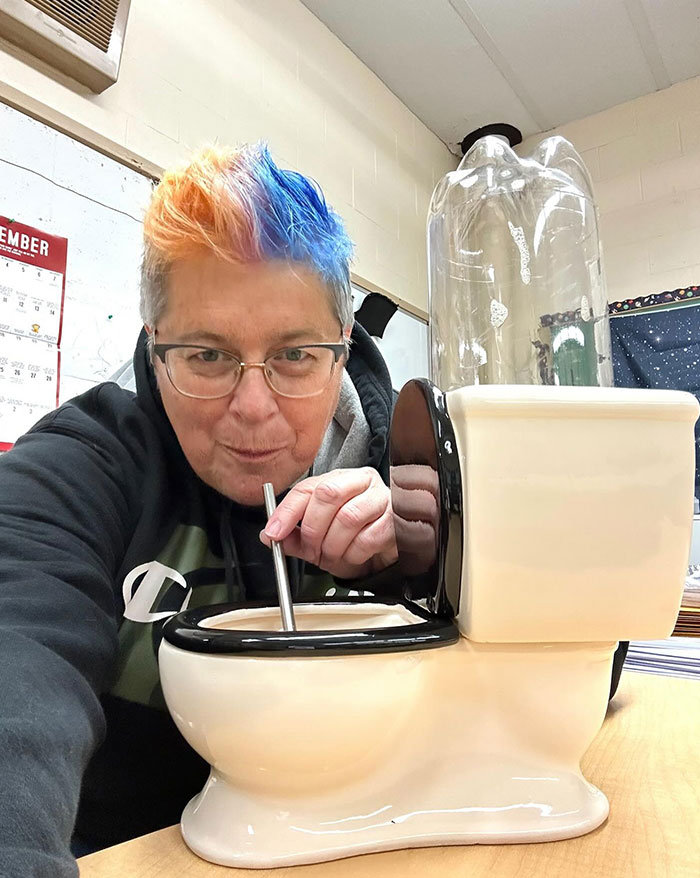 Person with colorful hair sipping with a metal straw from a creative toilet-shaped drink container, showcasing unique sippers.