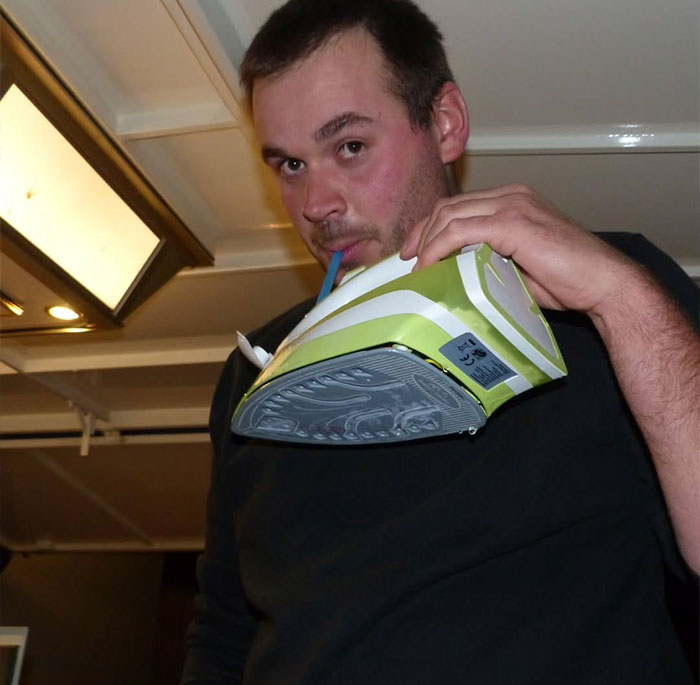 Man creatively sipping from an iron using a straw indoors, an example of outrageously creative sippers.