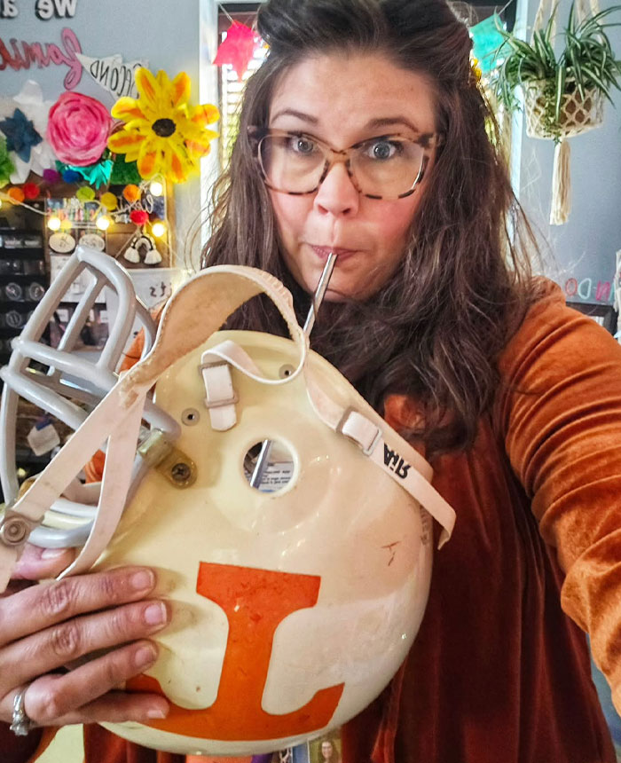 Woman drinking from a football helmet using a metal straw, showcasing creative sippers who chose to drink from anything but a cup.