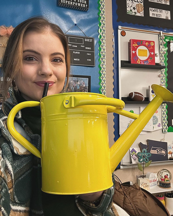 Woman sipping from a large yellow watering can, showcasing creative sippers who drink from anything but a cup.